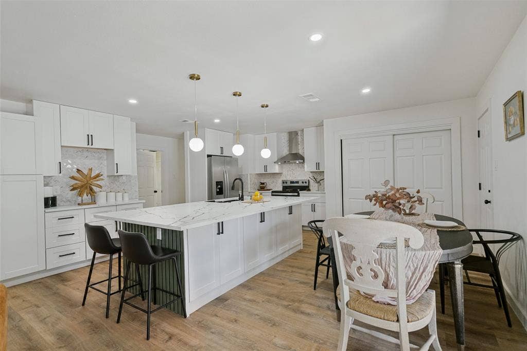 2704 Parkhaven Drive, Plano, TX 75075 Open-concept kitchen featuring white cabinetry, a large kitchen island with counter seating, a stainless steel refrigerator, and wood-finish flooring