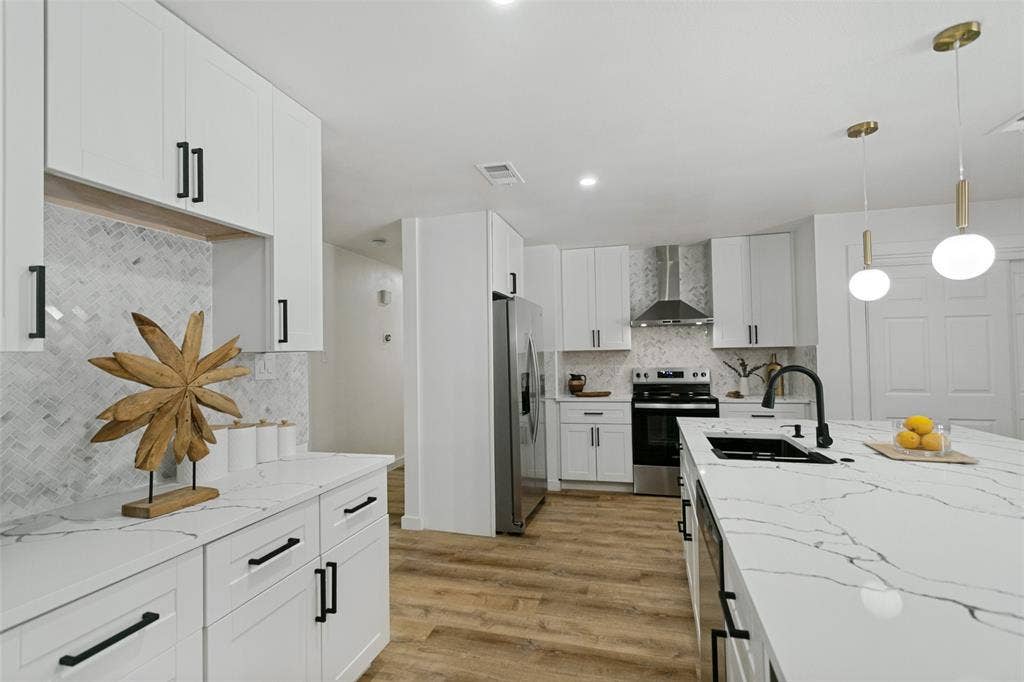 2704 Parkhaven Drive, Plano, TX 75075 Kitchen featuring white shaker-style cabinetry, a central island with a sink, stainless steel appliances, herringbone-patterned tile backsplash, and wood-finish flooring