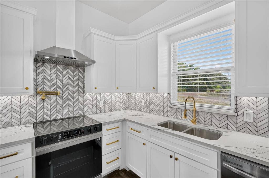 102 Shadywood Road, Trinidad, TX 75163 White shaker cabinetry with gold-tone hardware, chevron-patterned tile backsplash, stainless steel appliances, and a double basin sink with a gold-tone gooseneck faucet