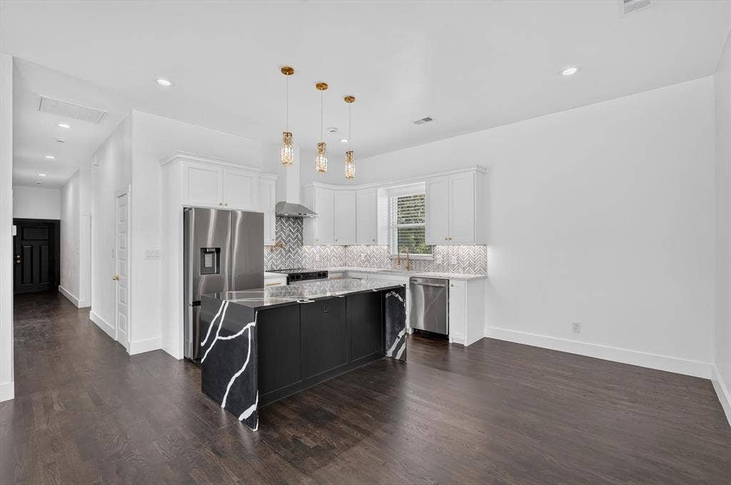 102 Shadywood Road, Trinidad, TX 75163 Kitchen featuring a central island with black cabinetry and a light-veined dark countertop, white upper and lower cabinetry, stainless steel appliances, and a chevron pattern tile backsplash