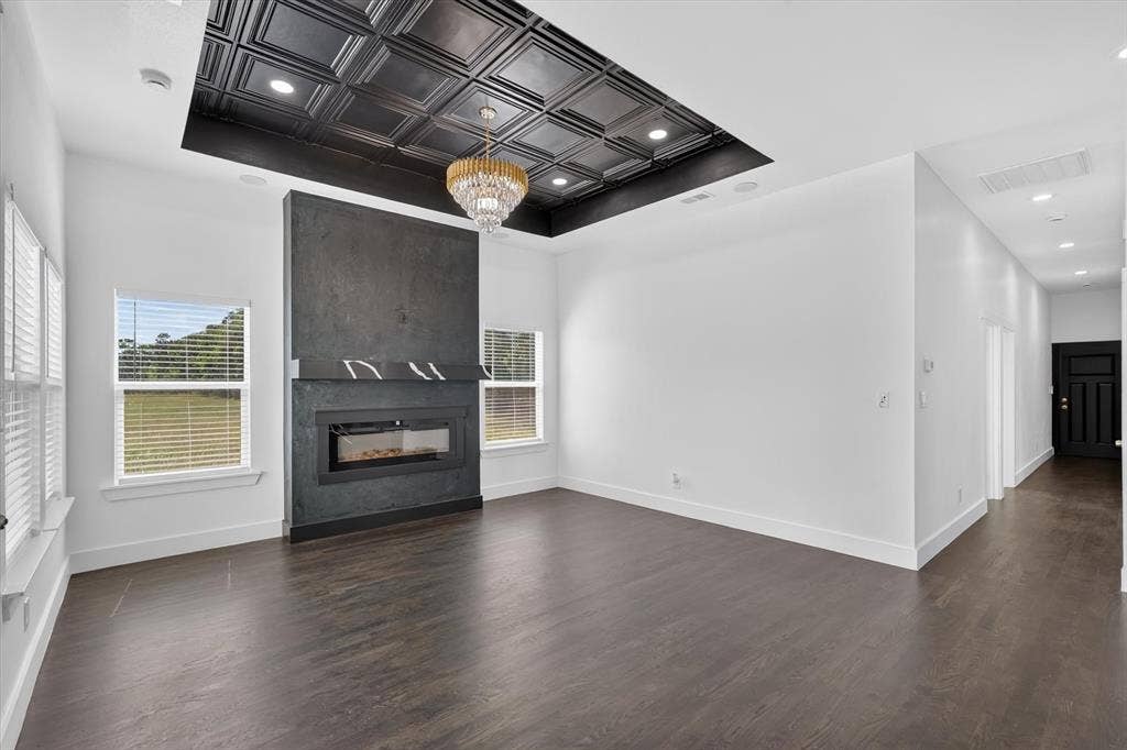 102 Shadywood Road, Trinidad, TX 75163 Recessed ceiling featuring a decorative chandelier, electric fireplace with dark-toned surround, two bright windows, and dark wood-finish flooring