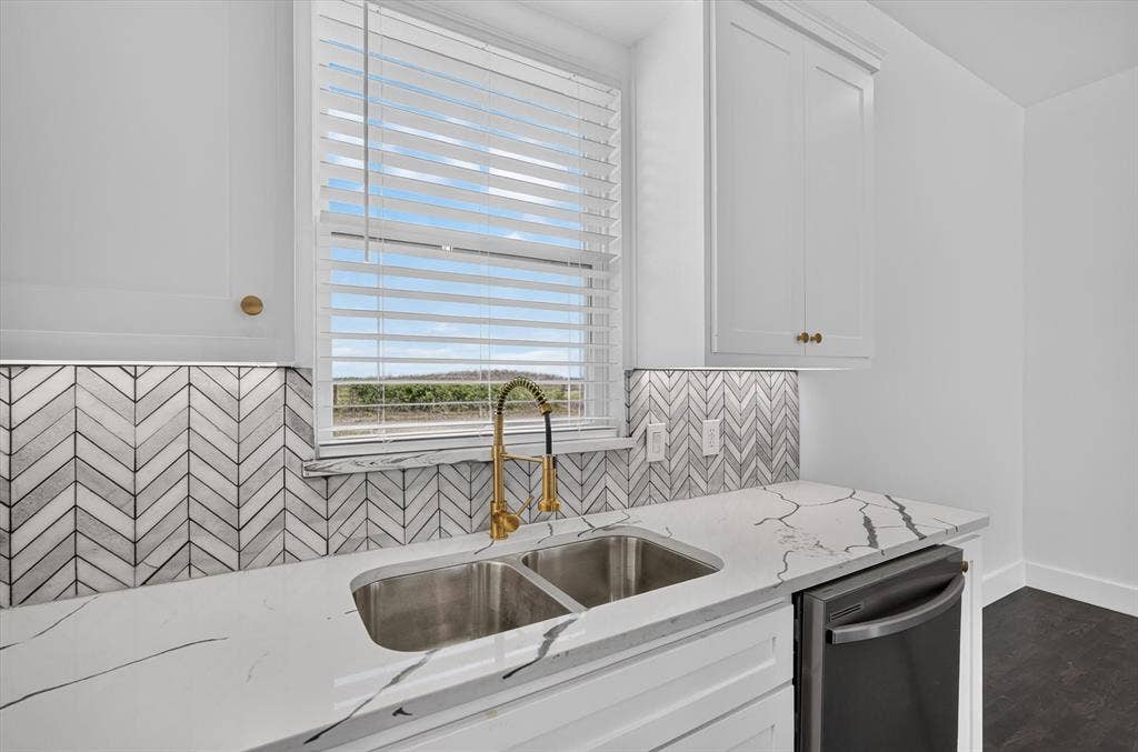 102 Shadywood Road, Trinidad, TX 75163 White cabinetry with gold-finish hardware, herringbone tile backsplash, stainless steel double basin sink, gold-finish gooseneck faucet, and white countertops with dark veining