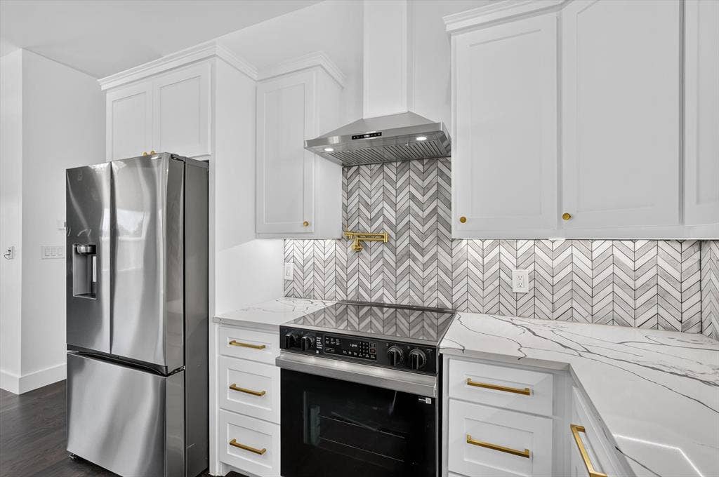 102 Shadywood Road, Trinidad, TX 75163 White shaker cabinetry with gold-tone hardware, stainless steel appliances, herringbone tile backsplash, and stone-finish countertops