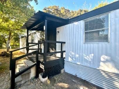 Covered porch with dark railing and steps, featuring corrugated metal siding and a window with blinds