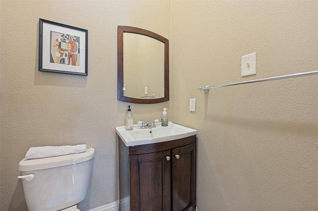 White toilet with a built-in tank, wood-finish vanity with dual-door storage, rectangular ceramic sink, and a wood-frame wall mirror