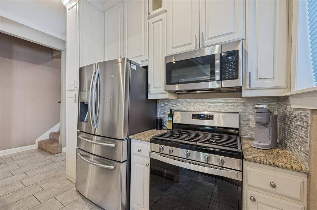 Stainless steel appliances, granite countertops, white cabinetry, tile backsplash, and tile flooring