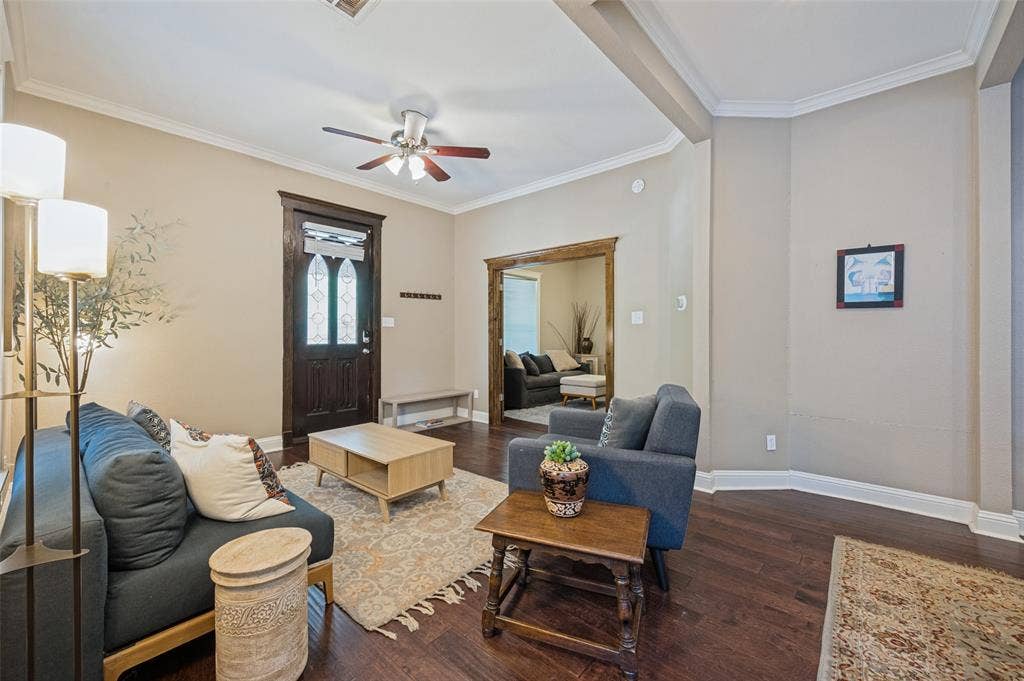 Wood-finish flooring throughout, featuring crown molding, a decorative front door with opaque glass, and a ceiling fan with integrated lighting