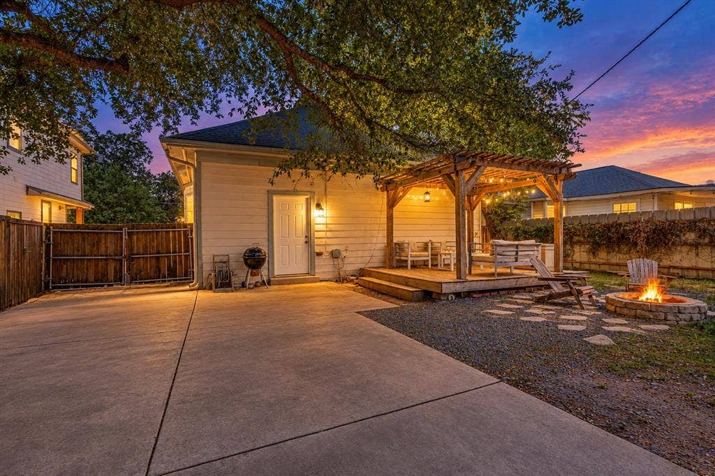 Expansive concrete driveway, wood privacy fencing, a wood deck with a pergola, and a stone fire pit area