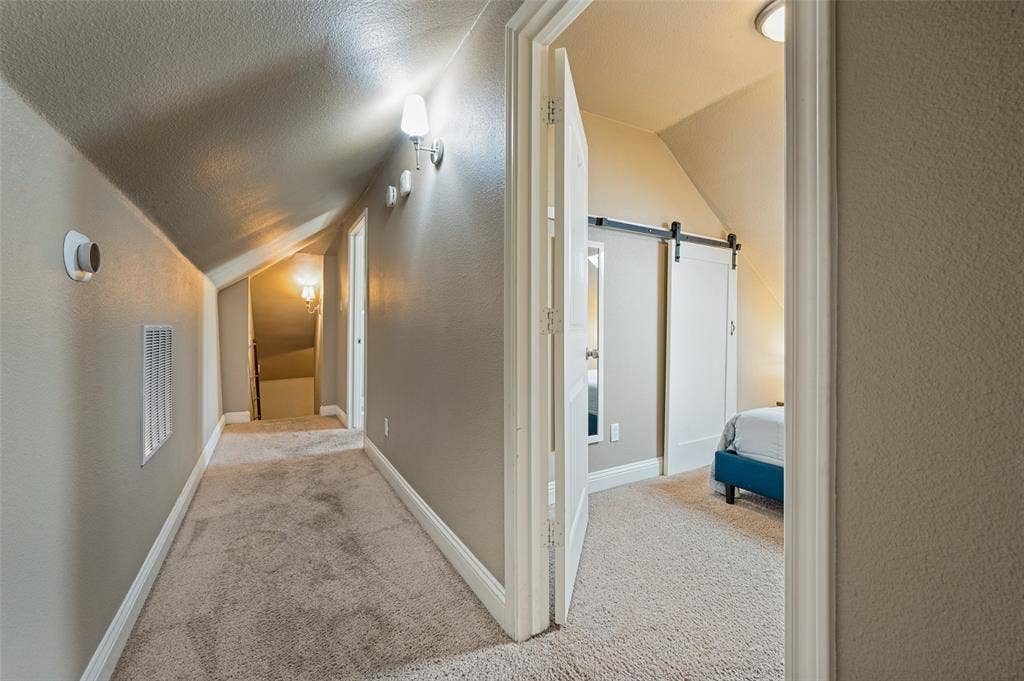 Carpeted hallway with sloped ceilings, white baseboards, and wall-mounted light fixtures
