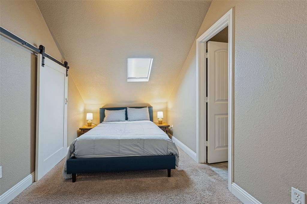 Vaulted ceiling room with an overhead skylight, a white barn door, and neutral-toned carpeting
