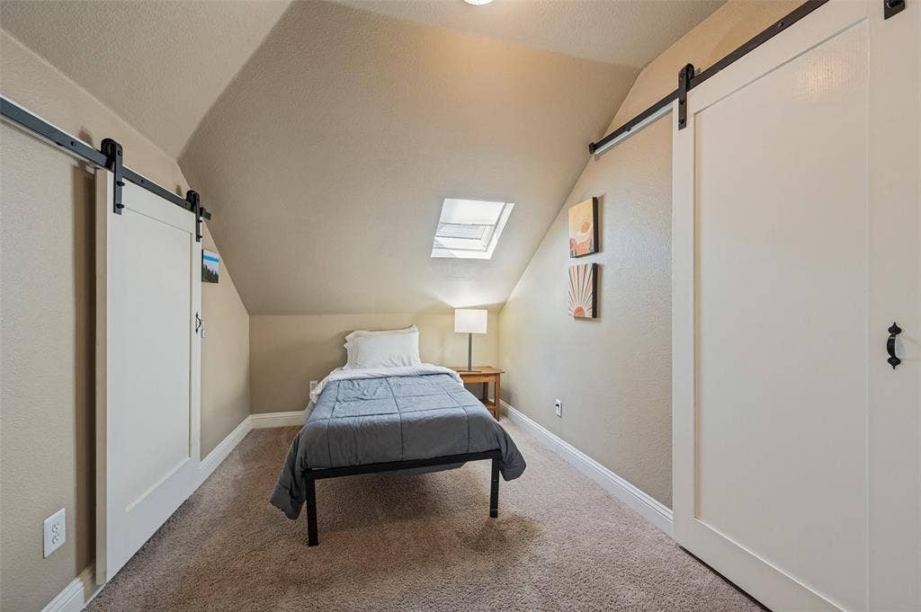 Sloped ceilings with a skylight, barn doors with black hardware, and wall-to-wall carpeting