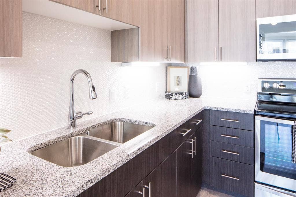 901 N Zang Boulevard, #204, Dallas, TX 75208 Kitchen with dark brown cabinets, stainless steel appliances, light stone countertops, and sink