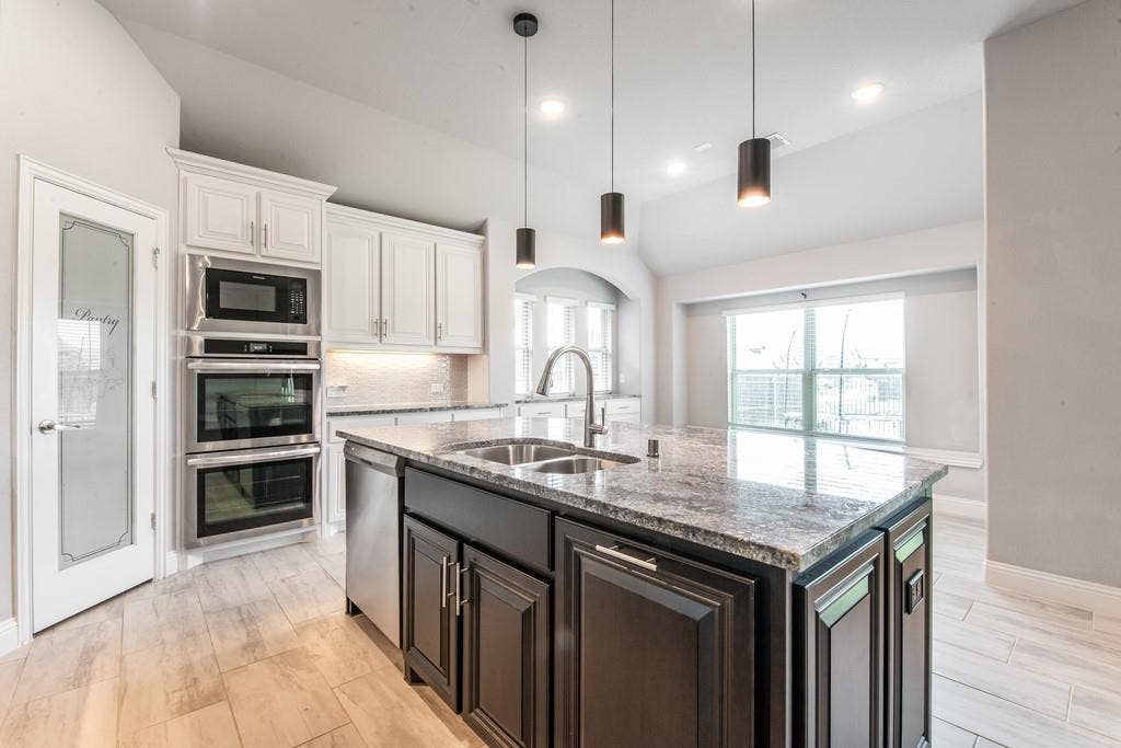 Kitchen featuring a large central island with a double basin sink, stainless steel appliances, white cabinetry, and wood-finish flooring