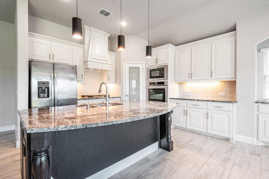 Kitchen with white cabinetry, stainless steel appliances, a large island with a stone countertop, and tile flooring