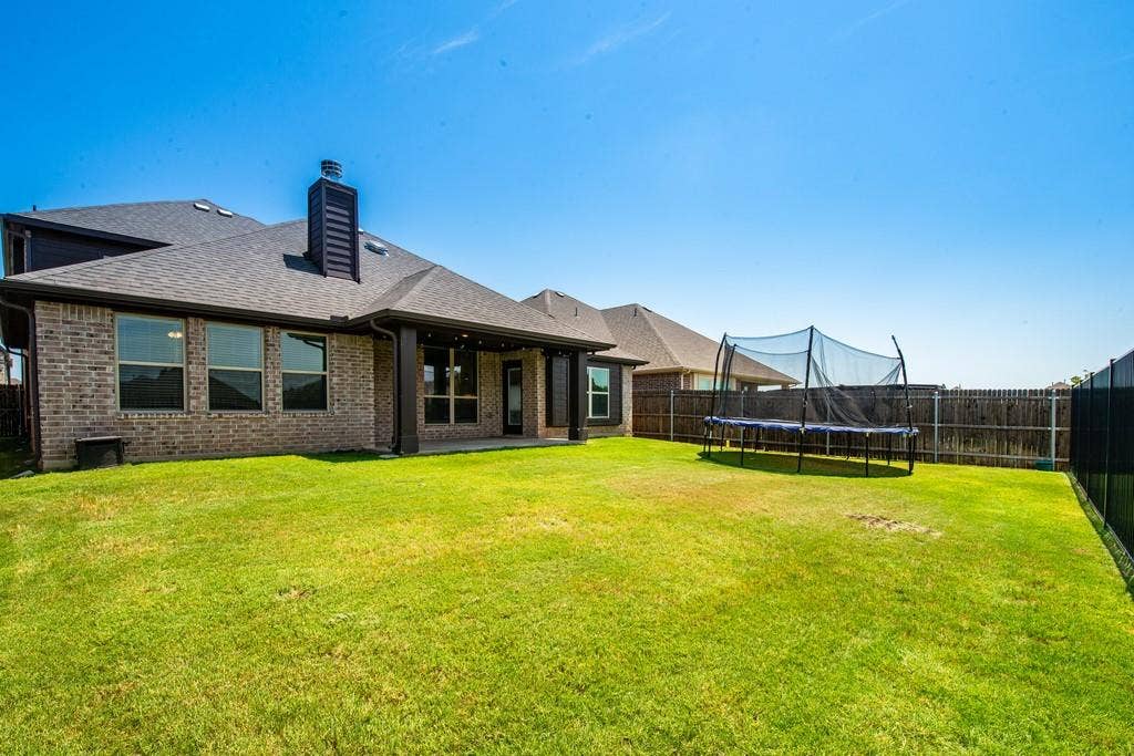 Spacious backyard featuring a covered patio, brick exterior, multiple windows, and a privacy fence