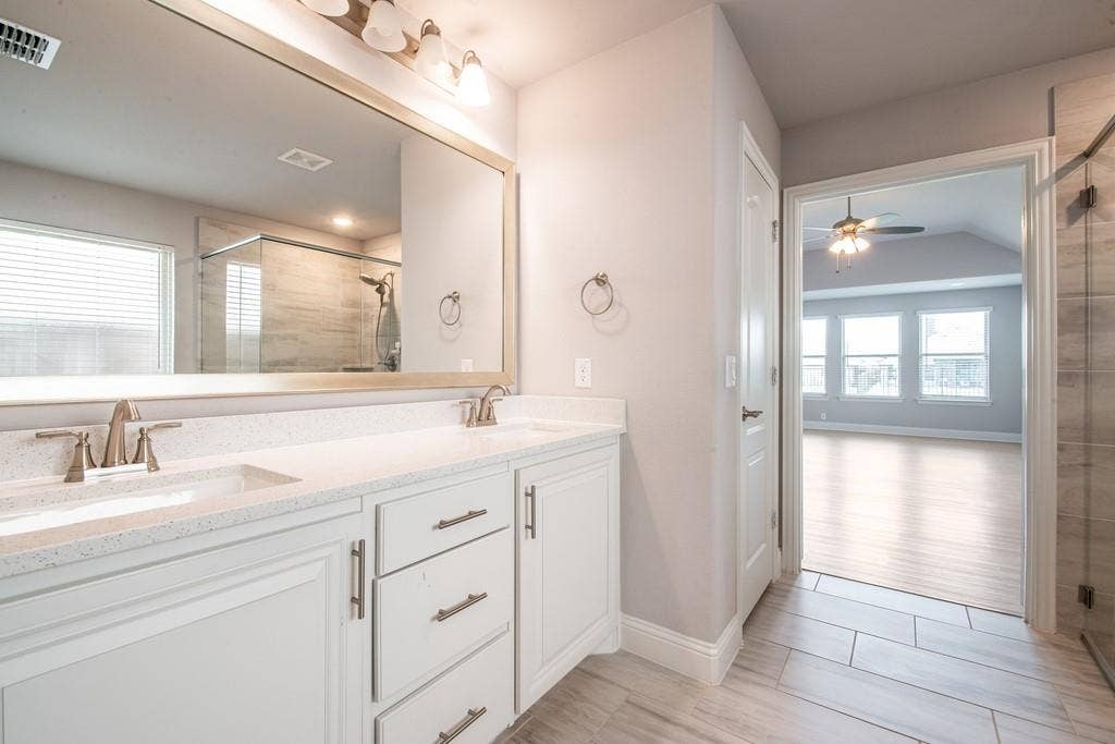 Dual vanity with white cabinetry and brushed nickel hardware, expansive mirror, and integrated shower with sliding glass door