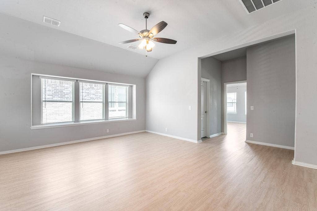 Spacious room featuring vaulted ceilings, wood-finish flooring, a contemporary ceiling fan with integrated lighting, and a multi-panel window