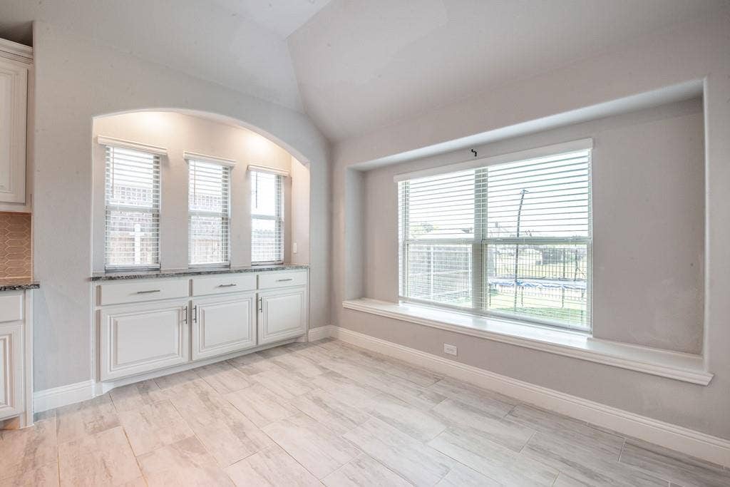Built-in cabinetry with granite countertop, arched architectural detail, multiple windows, and wood-finish flooring