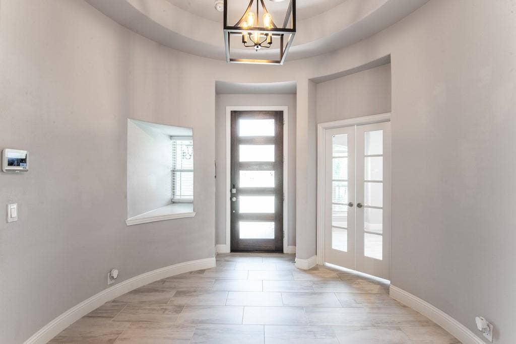 Curved entryway with tile flooring, a modern chandelier, a dark wood entry door with horizontal glass panels, and double French doors