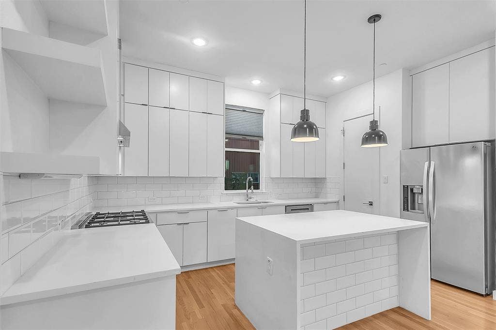 1510 N Washington Avenue, #703, Dallas, TX 75204 Kitchen in this Dallas condo with full-height white cabinets, waterfall island, gas range and stainless refrigerator