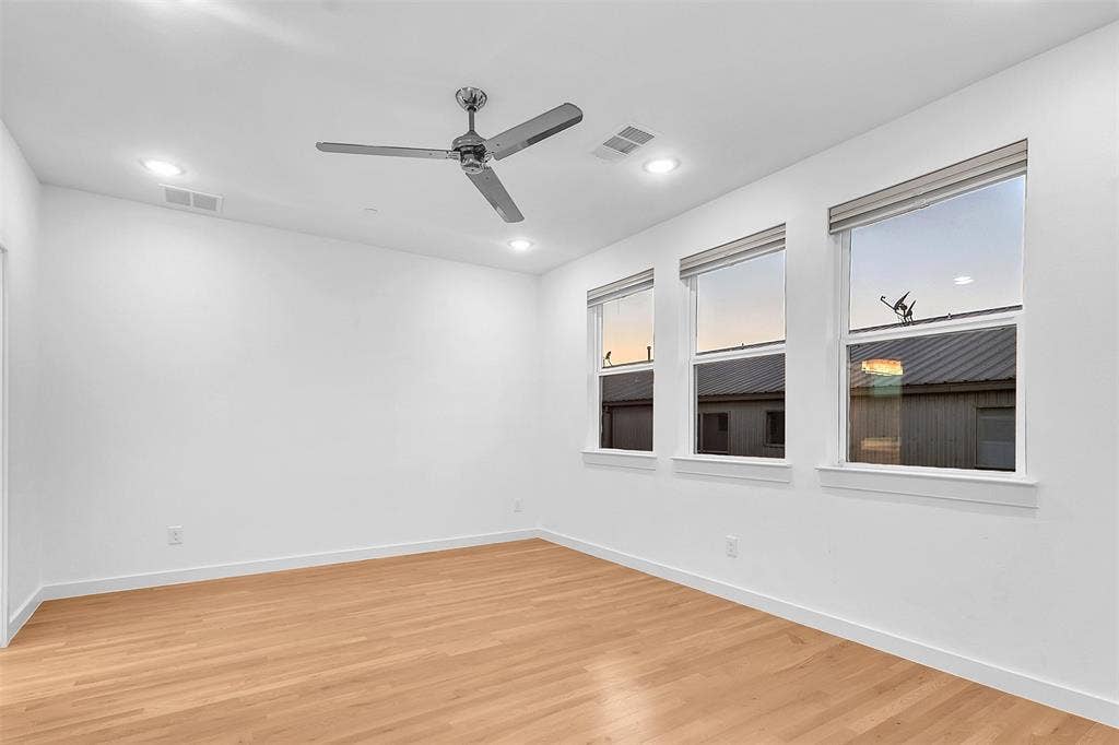 1510 N Washington Avenue, #703, Dallas, TX 75204 Spacious bedroom with three shaded windows, recessed lighting, a chrome ceiling fan and wood-look floors