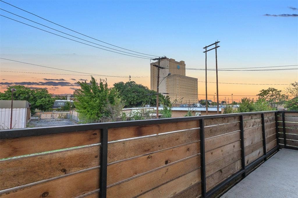 1510 N Washington Avenue, #703, Dallas, TX 75204 Corner of the wood-railed balcony at sunset, looking out over nearby rooftops and trees in East Dallas