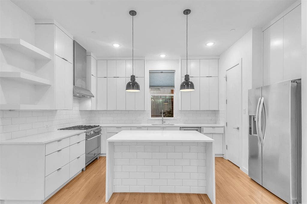 1510 N Washington Avenue, #703, Dallas, TX 75204 Straight-on view of the kitchen with two pendant lights over the waterfall island, open shelves and refrigerator