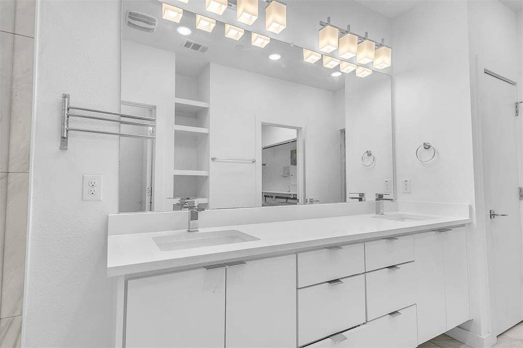 1510 N Washington Avenue, #703, Dallas, TX 75204 Primary bath in this Dallas condo with a long white vanity, dual undermount sinks, wide mirror and open shelving