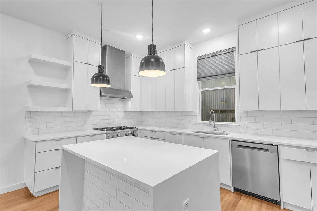 1510 N Washington Avenue, #703, Dallas, TX 75204 White kitchen with a waterfall island, stainless dishwasher, gas range, pendant lights and full-height cabinetry