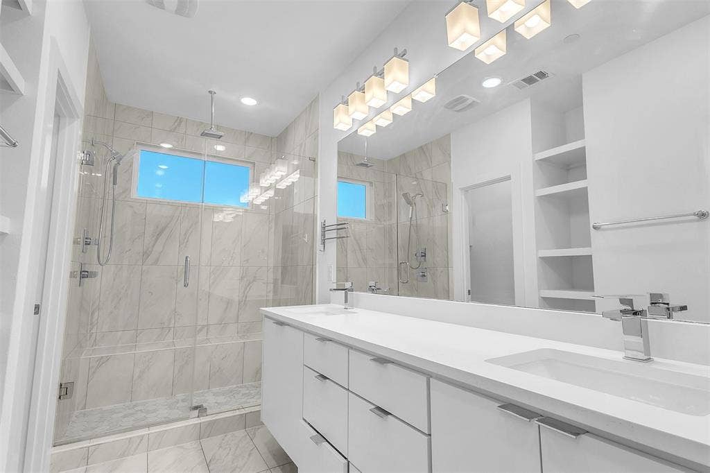 1510 N Washington Avenue, #703, Dallas, TX 75204 Primary bath with a glass-enclosed walk-in shower, dual-sink white vanity, wide mirror and marble-look tile