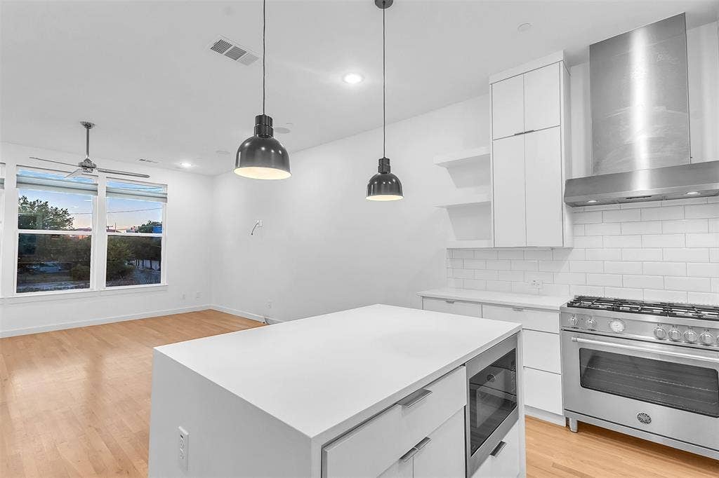 1510 N Washington Avenue, #703, Dallas, TX 75204 Kitchen island with a built-in microwave, plus a commercial-style gas range, stainless vent hood and open shelves