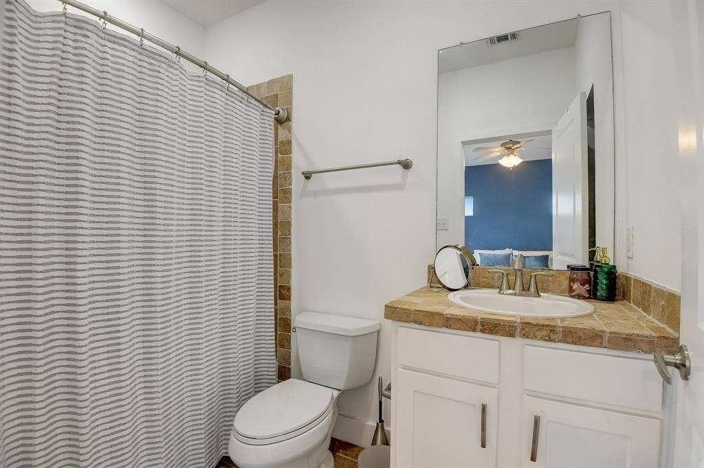 Bathroom with vanity, toilet, ceiling fan, and curtained shower