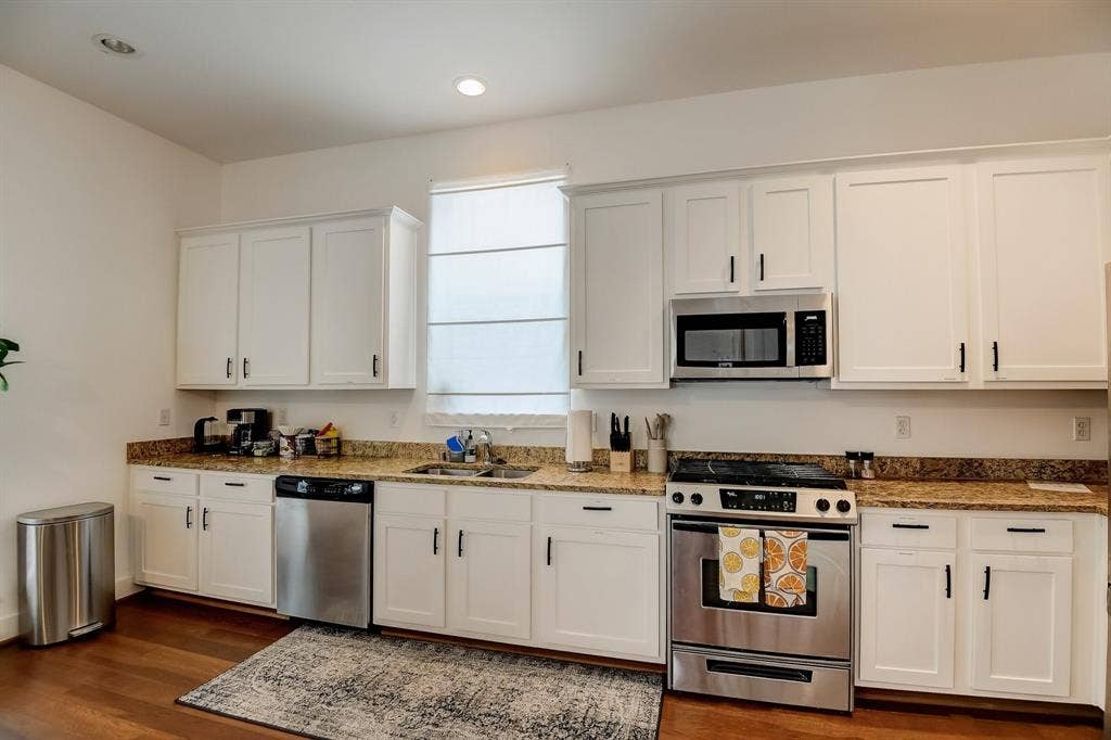 Kitchen featuring stainless steel appliances, a sink, dark wood-type flooring, white cabinets, and stone countertops
