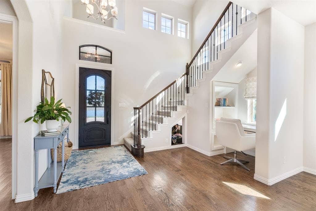 Hardwood flooring throughout the entry, iron baluster staircase, a built-in desk with shelving, and high ceilings with transom windows