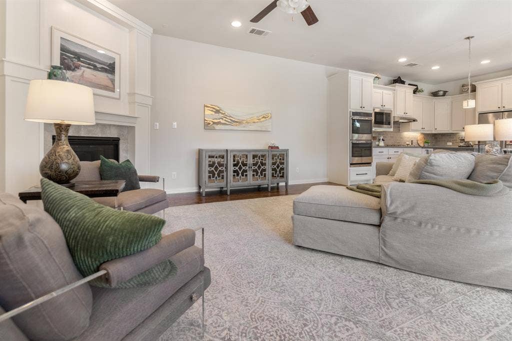 Hardwood-style flooring, white built-in cabinetry, recessed lighting, ceiling fan, and a fireplace with a stone surround