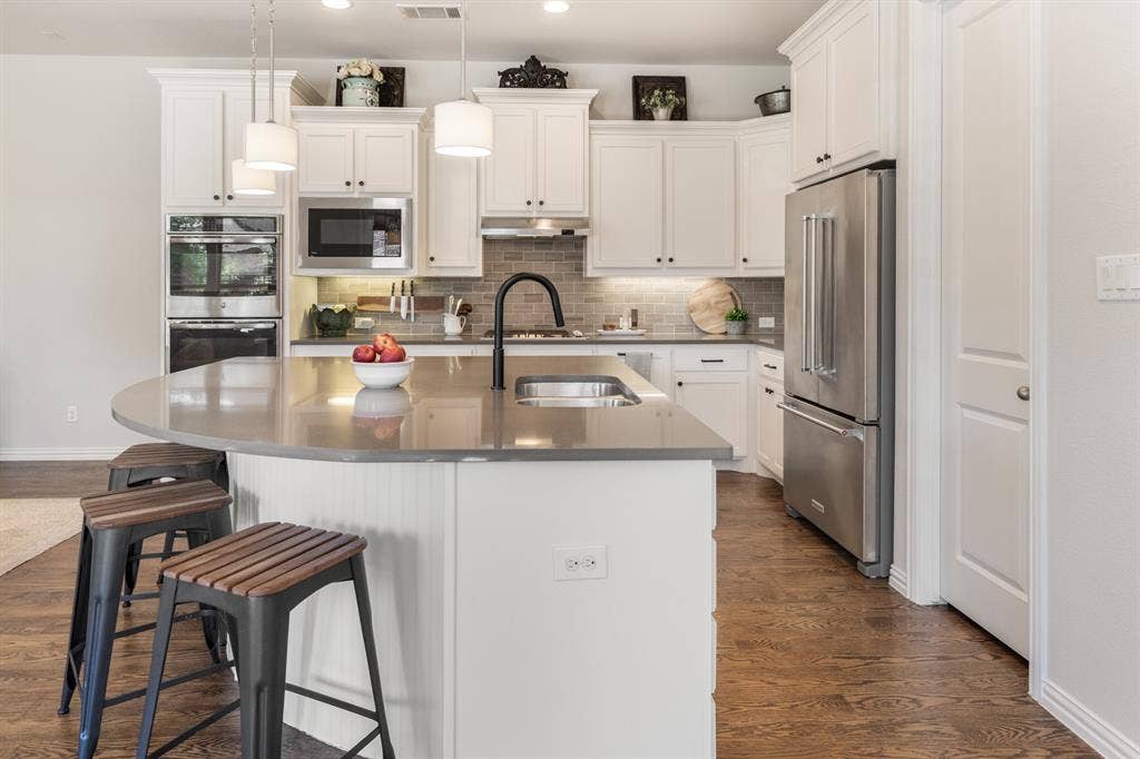 Kitchen featuring white cabinetry, stainless steel appliances, a center island with a sink, pendant lighting, and wood-finish flooring