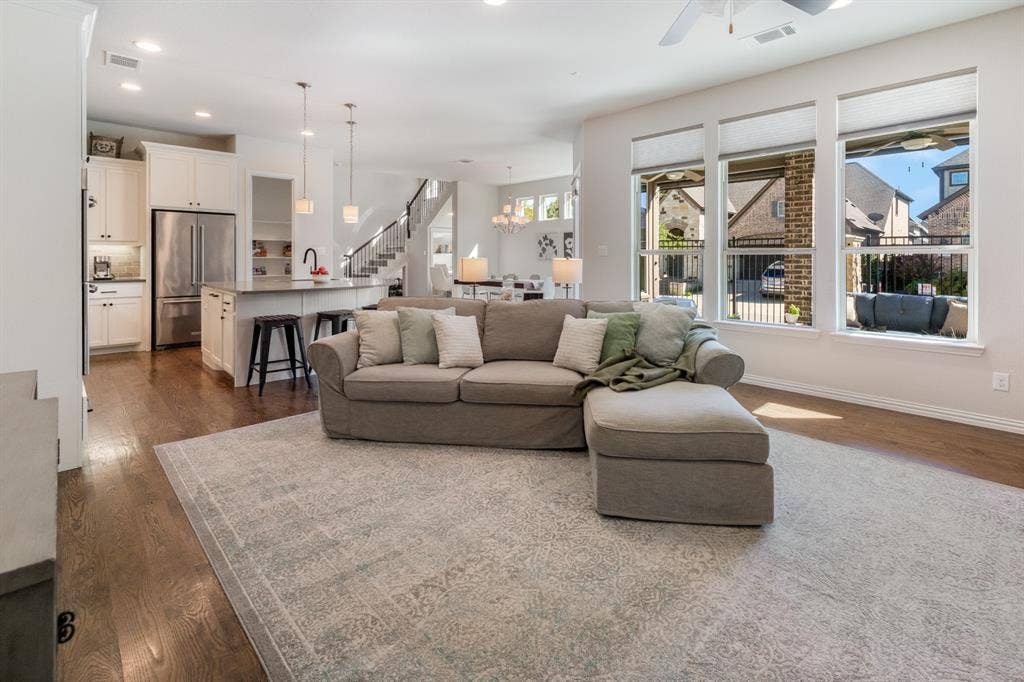 Open-concept living area featuring wood-finish flooring, a kitchen island with seating, white cabinetry, stainless steel appliances, and a wall of windows