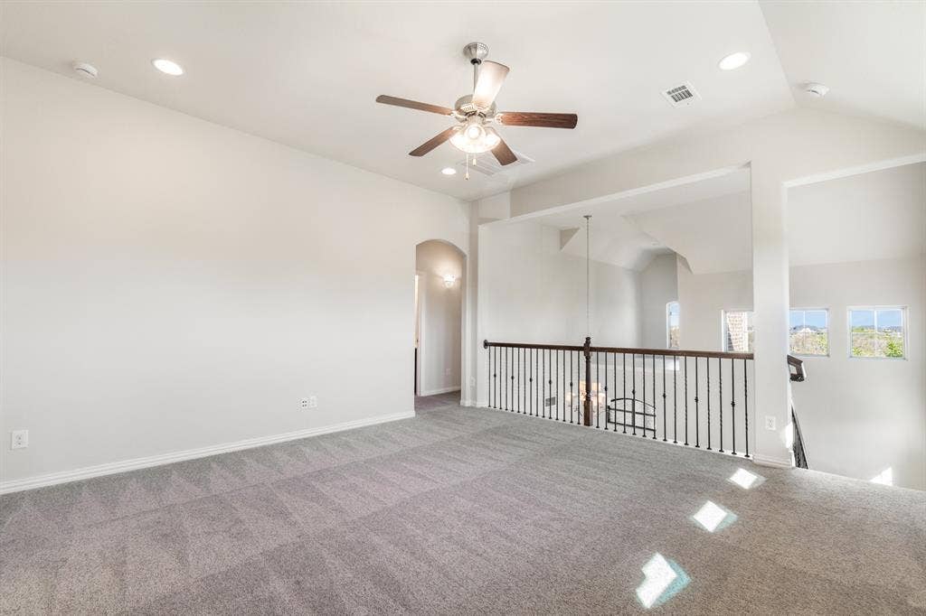 Expansive carpeted loft with recessed lighting, ceiling fan, and wrought iron balustrade