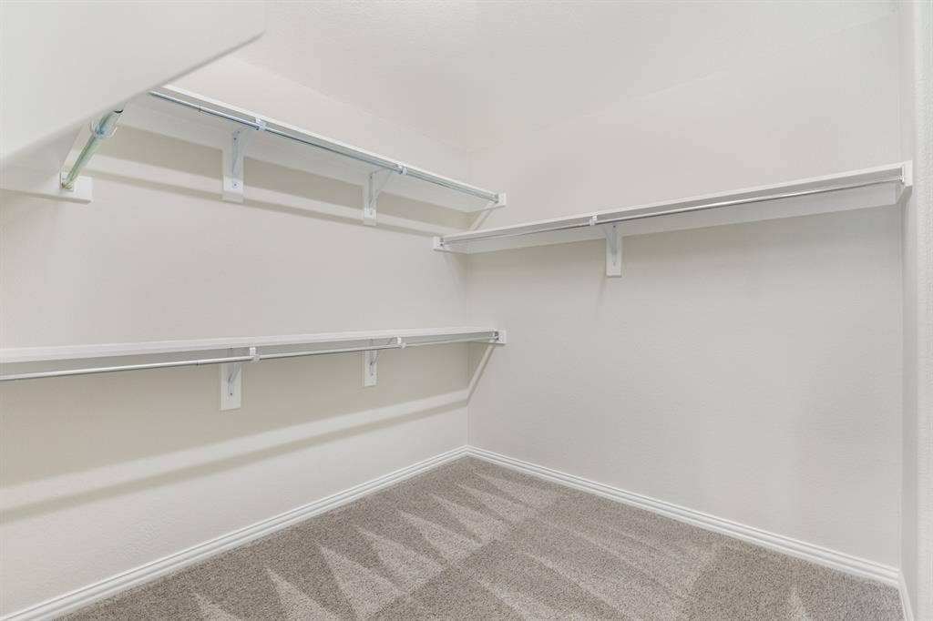 Primary room. Built-in shelving with hanging rods and neutral tone carpeting