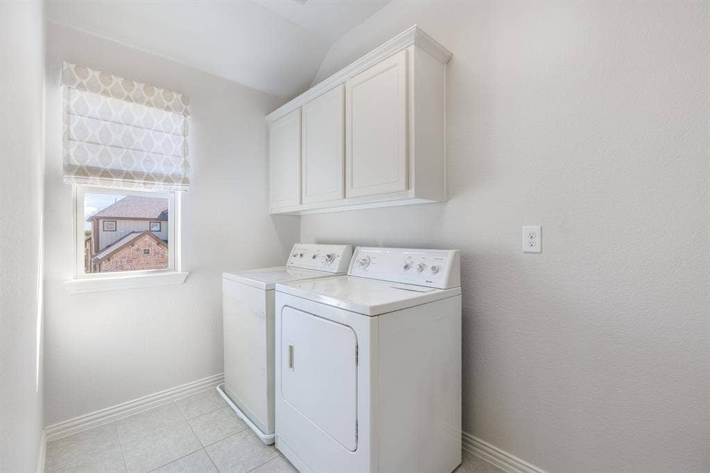 White shaker-style cabinetry with crown molding, a window with a patterned Roman shade, and tiled flooring