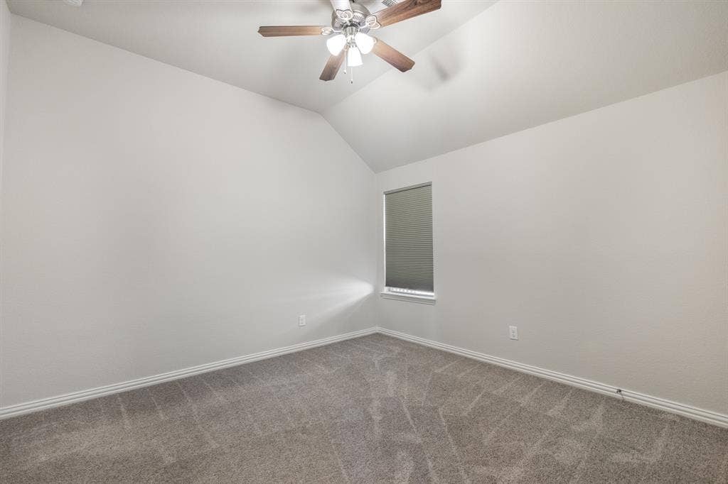 Upstairs, third bedroom with vaulted ceiling featuring a ceiling fan, neutral wall paint, gray carpet, and a window with a roller shade
