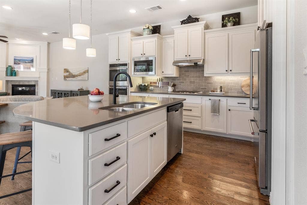 Kitchen featuring a center island with sink, white shaker cabinetry, stainless steel appliances, and wood-finish flooring