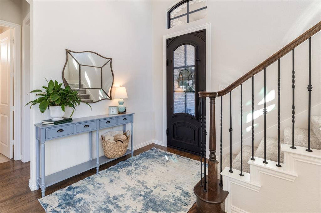 Arched entryway door with glass paneling, overhead transom window, wood-finish flooring, and a carpeted staircase with wrought iron balusters and a wood handrail