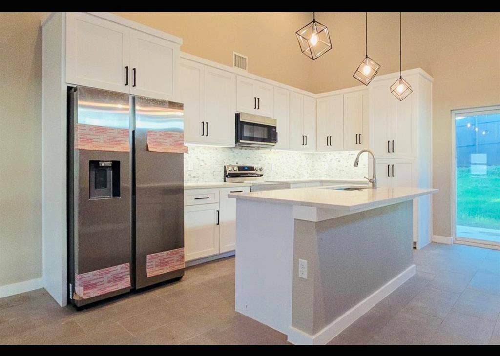 2821 Avenue L, Fort Worth, TX 76105 Kitchen featuring white cabinetry, stainless steel appliances, a center island with sink, tile flooring, and vaulted ceilings