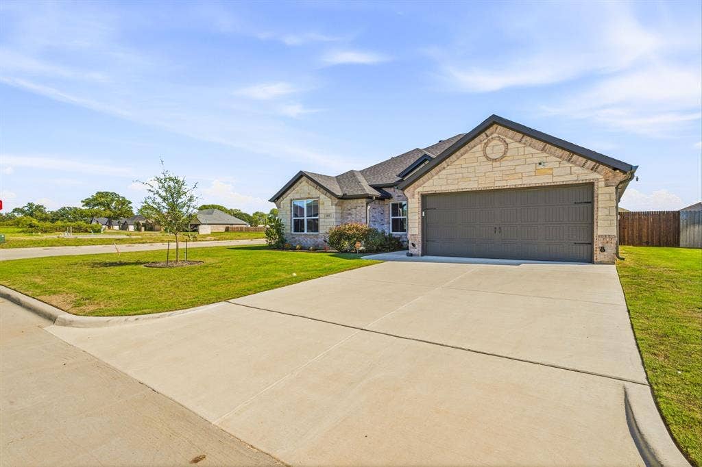 601 Violet Drive, Tolar, TX 76476 Stone facade with a dark gray garage door, concrete driveway, and a manicured lawn