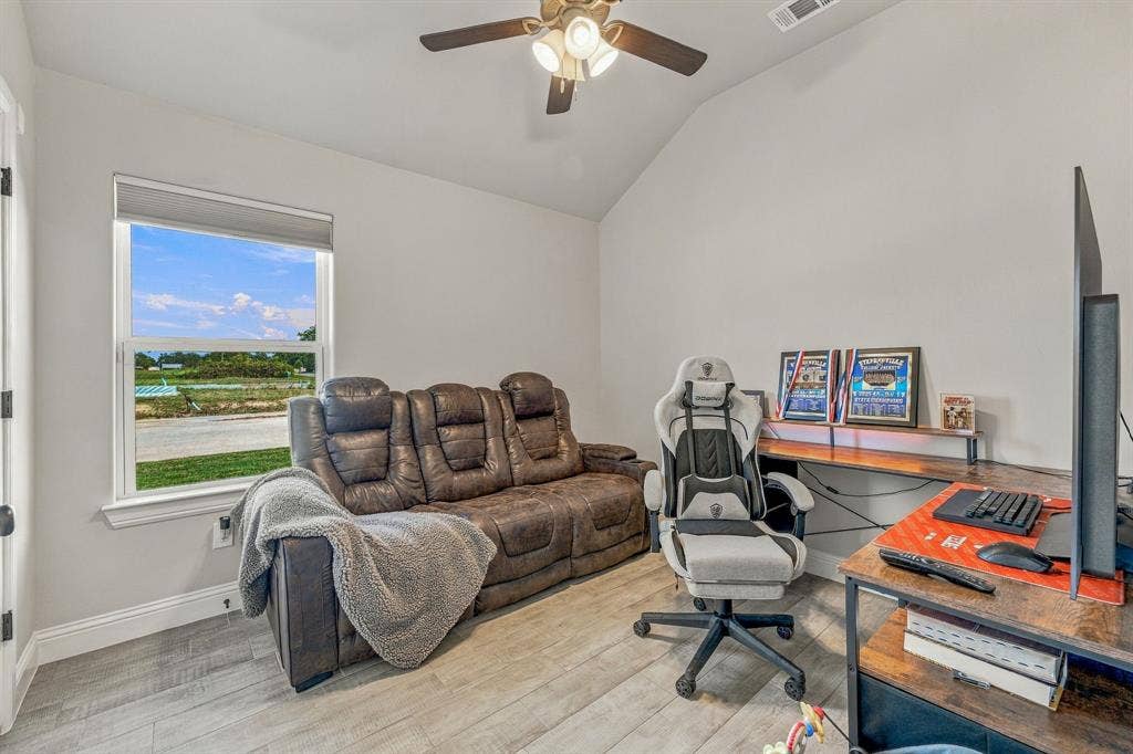 601 Violet Drive, Tolar, TX 76476 Vaulted ceiling with a ceiling fan, light gray wall paint, wood-finish flooring, and a window with roller shade