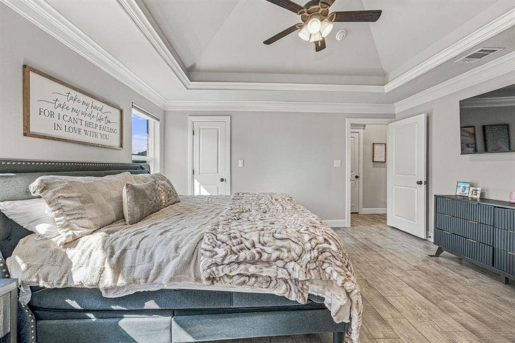601 Violet Drive, Tolar, TX 76476 Tray ceiling with crown molding, wood-finish flooring, ceiling fan with integrated lighting, and multiple doors with dark hardware