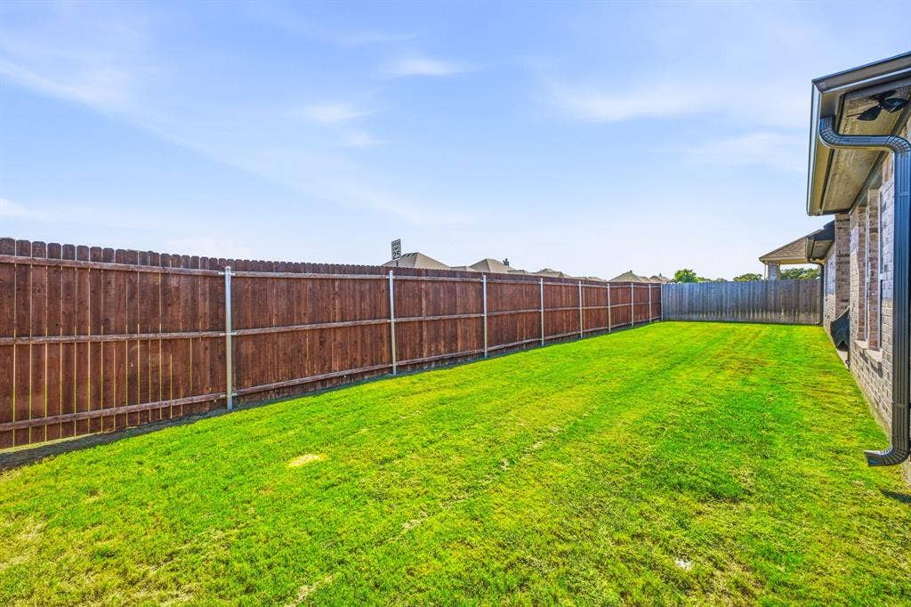 601 Violet Drive, Tolar, TX 76476 Expansive backyard featuring a manicured lawn, full wood privacy fencing, and a brick exterior with a dark rain gutter system