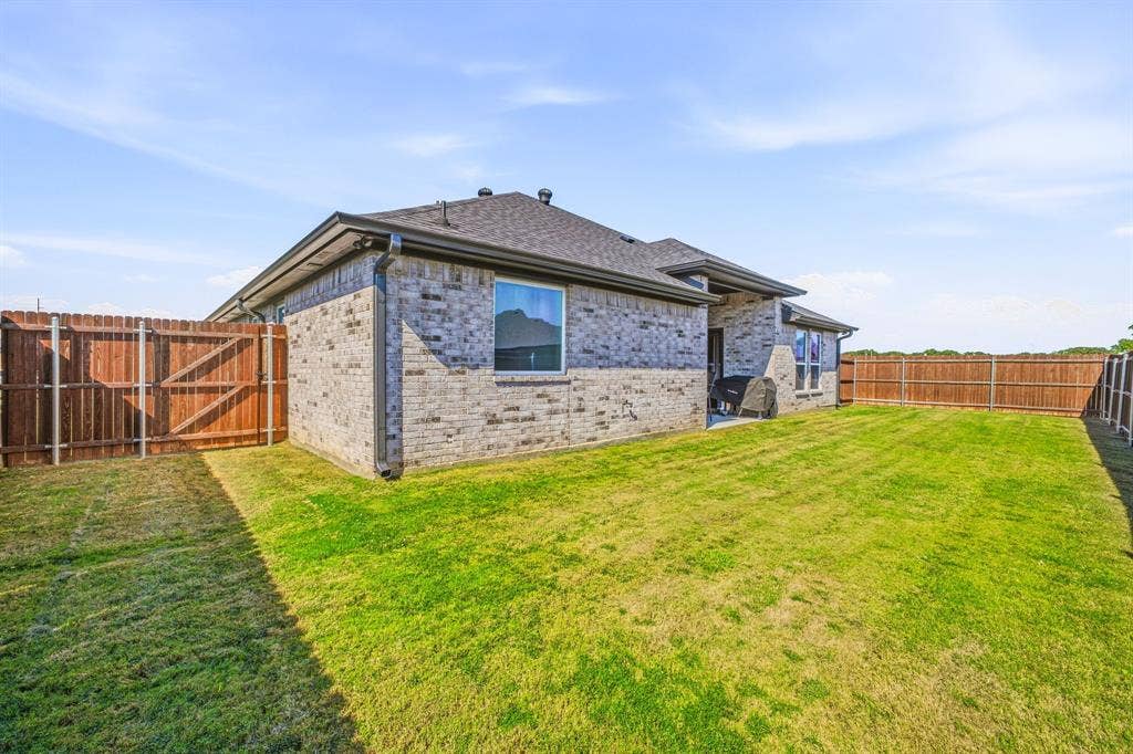 601 Violet Drive, Tolar, TX 76476 Expansive backyard featuring a manicured lawn, full privacy fencing, and a brick exterior home with a shingled roof