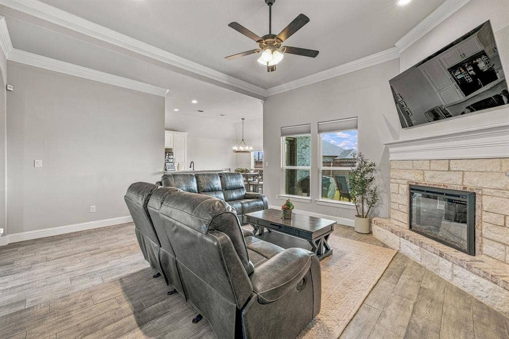 601 Violet Drive, Tolar, TX 76476 Spacious living area featuring wood-finish flooring, a stone-clad fireplace with a mantel, and crown molding accents